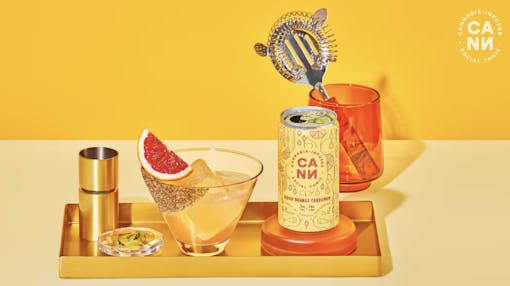 LGBTQIA+ brands and dispensaries like CANN social tonics, pictured here with a mini can of their Blood Orange Cardamom with a cocktail glass featuring a THC mocktail and slice of blood orange